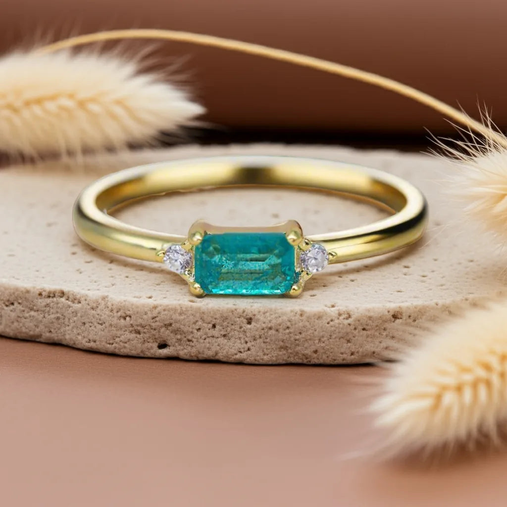 Gold ring with a green gemstone on a textured surface with dried plants.