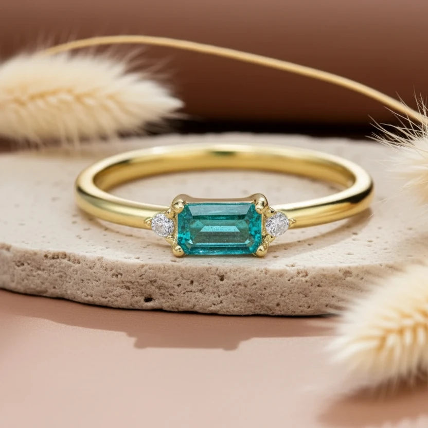 Gold ring with a green gemstone on a textured surface with dried plants.