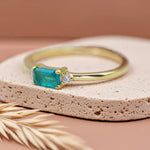 Gold ring with a green gemstone on a beige stone surface