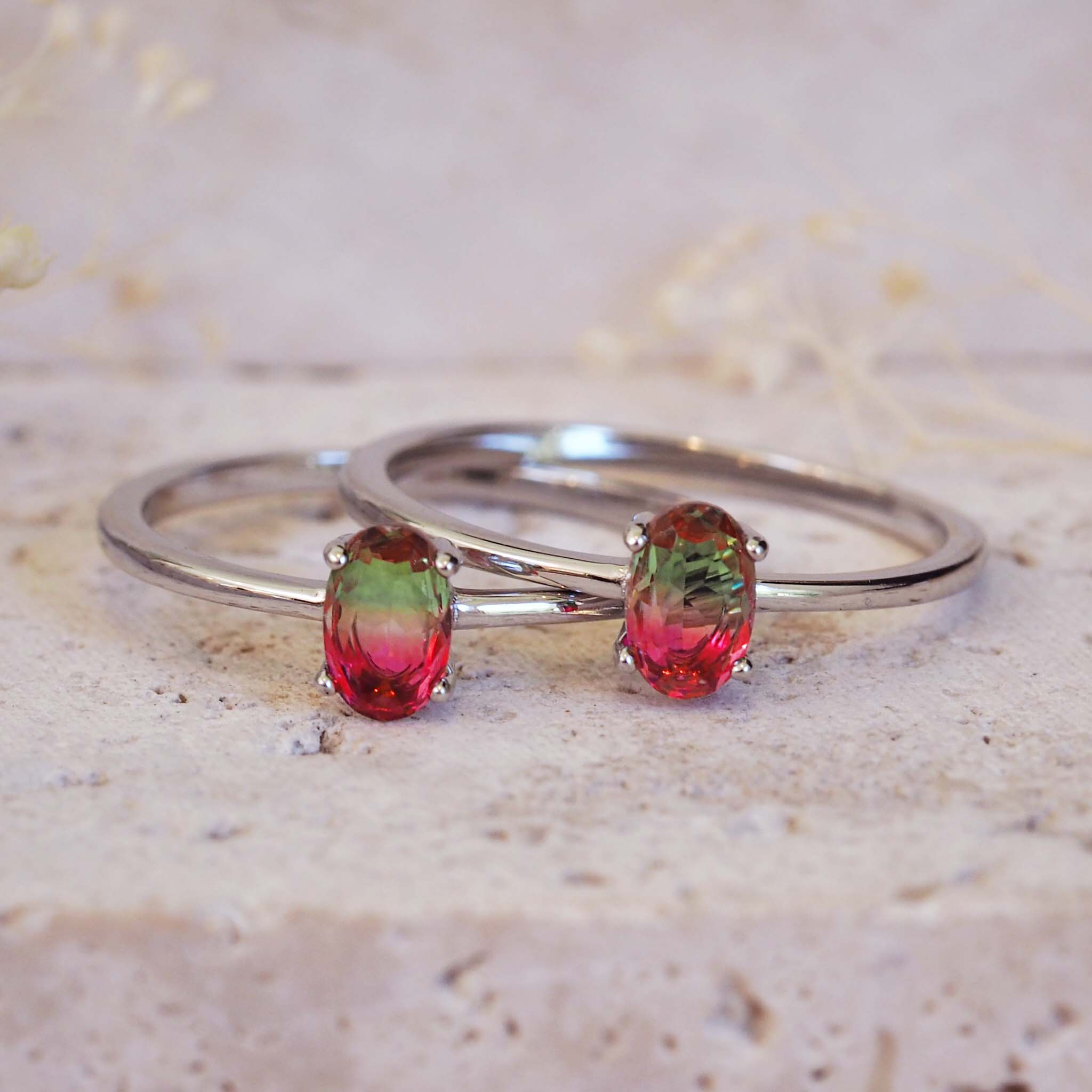 Silver ring with red and green gemstones on a textured beige surface