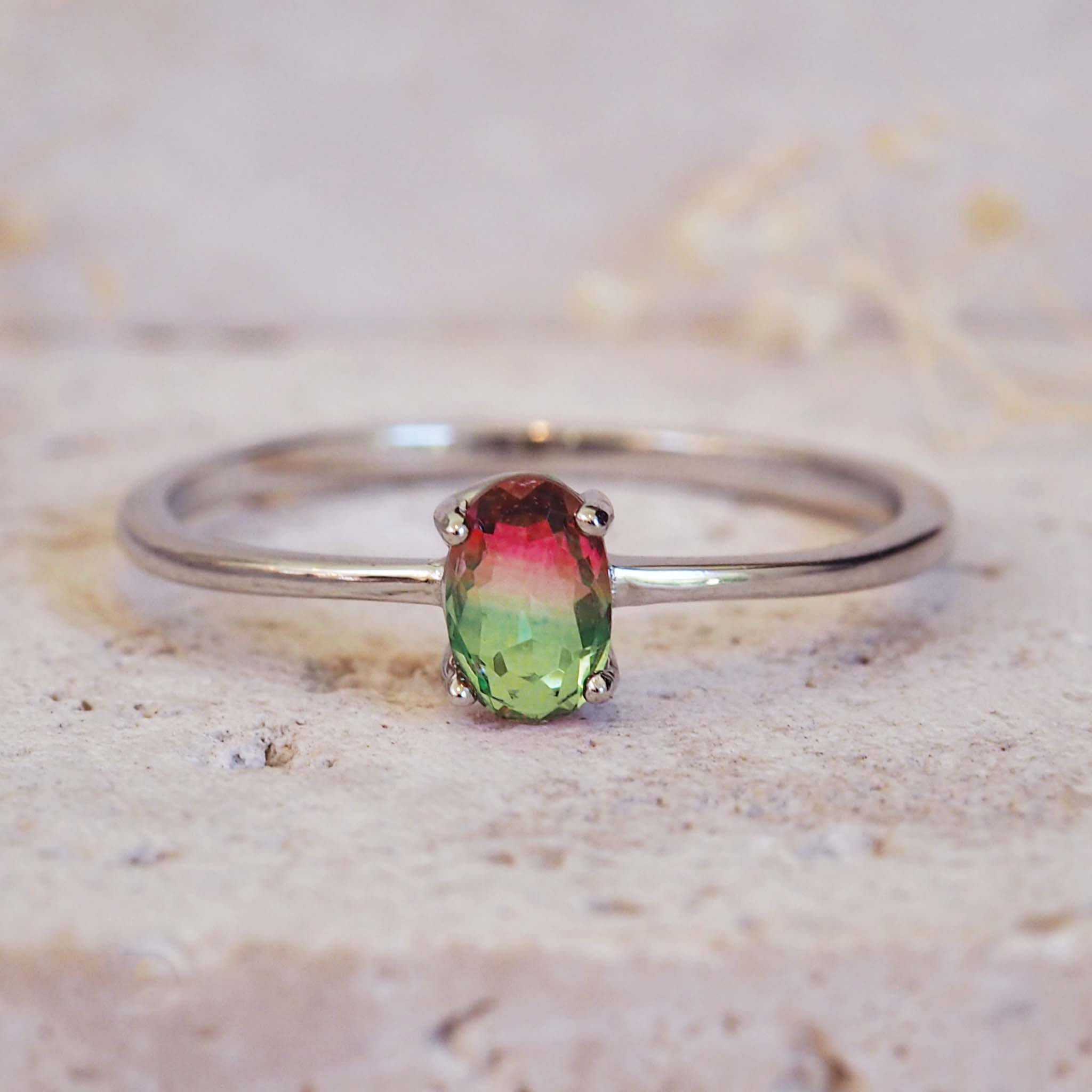 Silver ring with a multicolored gemstone on a textured beige surface