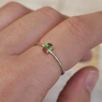 Silver ring with a green gemstone on a person's finger against a neutral background
