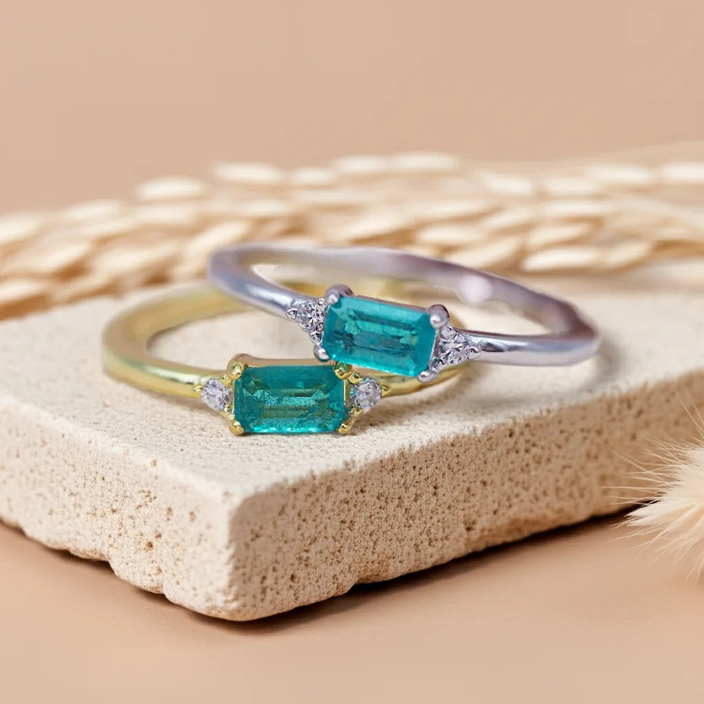 Two emerald-cut gemstone rings on a textured beige surface