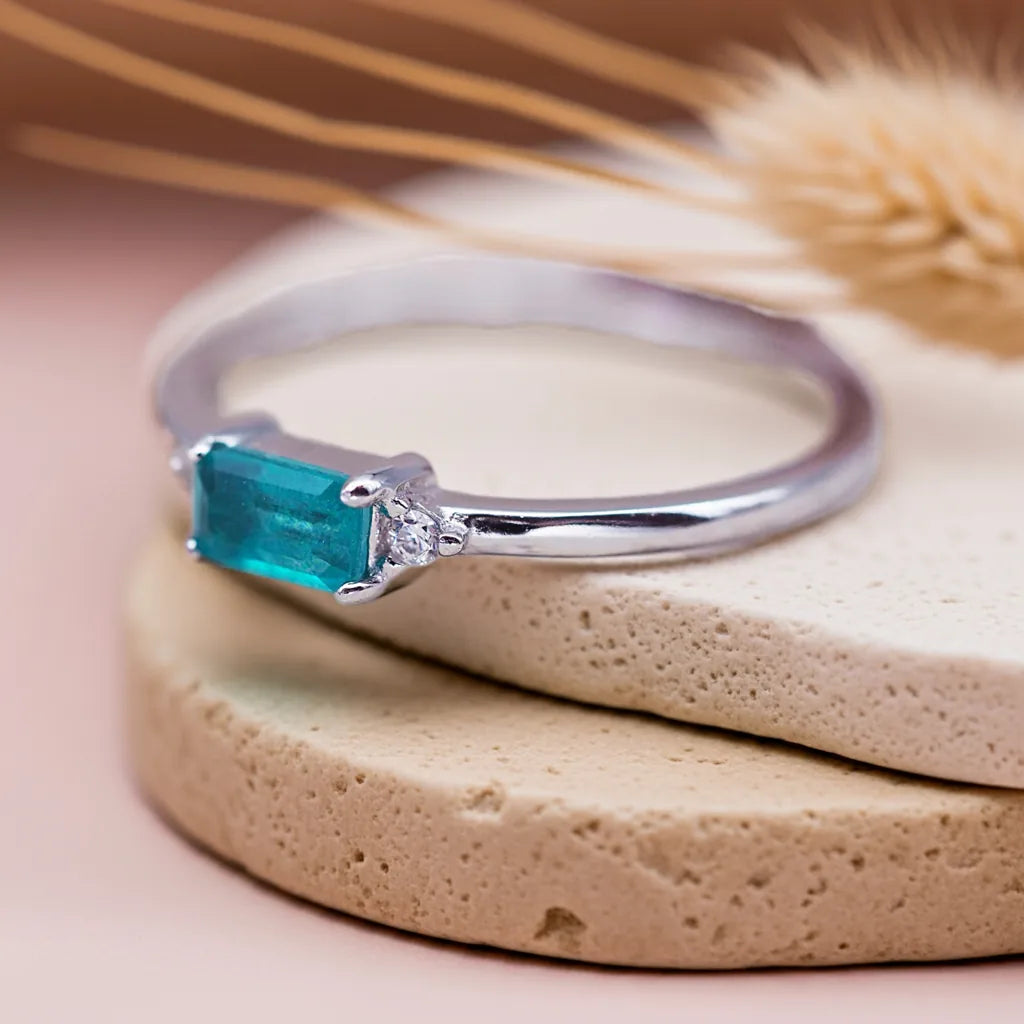 Silver ring with a blue gemstone on a beige stone surface with dried grass in the background