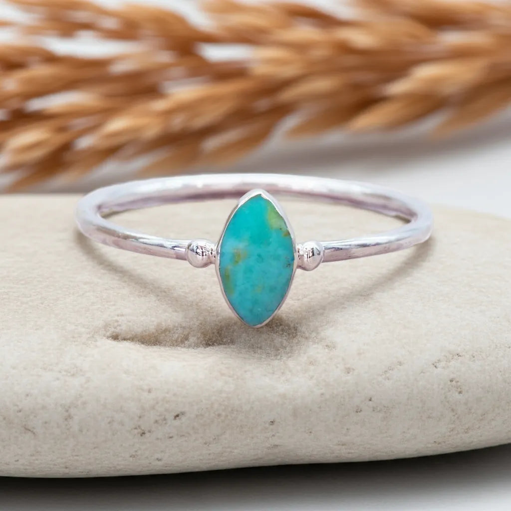Silver ring with a turquoise stone on a beige surface with dried grass in the background