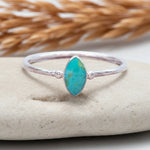 Silver ring with a turquoise stone on a beige surface with dried grass in the background