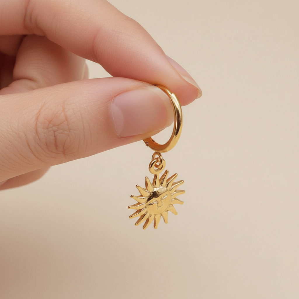 Gold hoop earring with a sun-shaped pendant held by a hand against a beige background