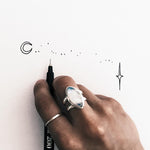 Hand with a ring holding a pen, drawing simple line art on a white background
