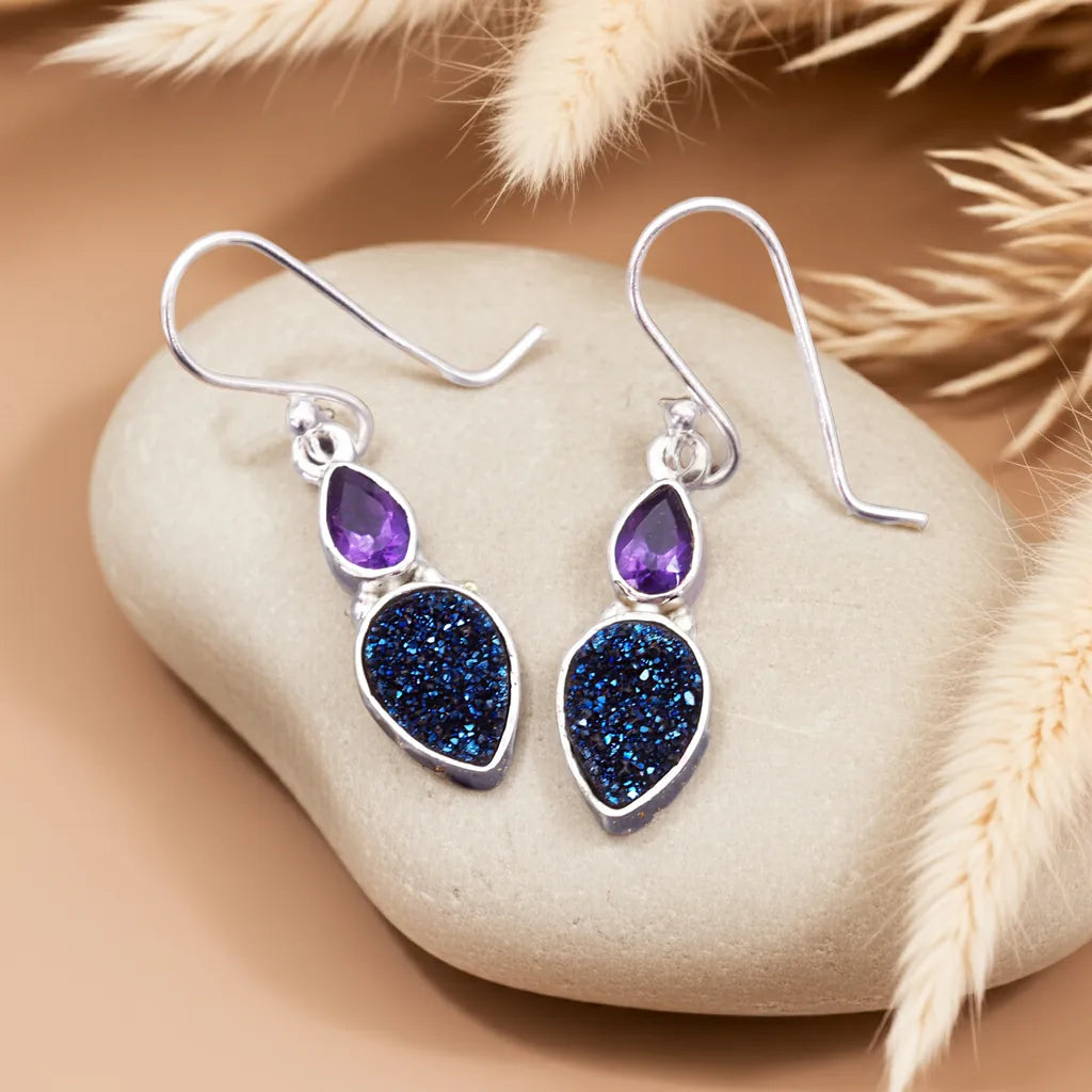 Silver earrings with purple and blue stones on a stone surface