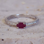 Silver ring with a red gemstone and diamond accents on a textured surface