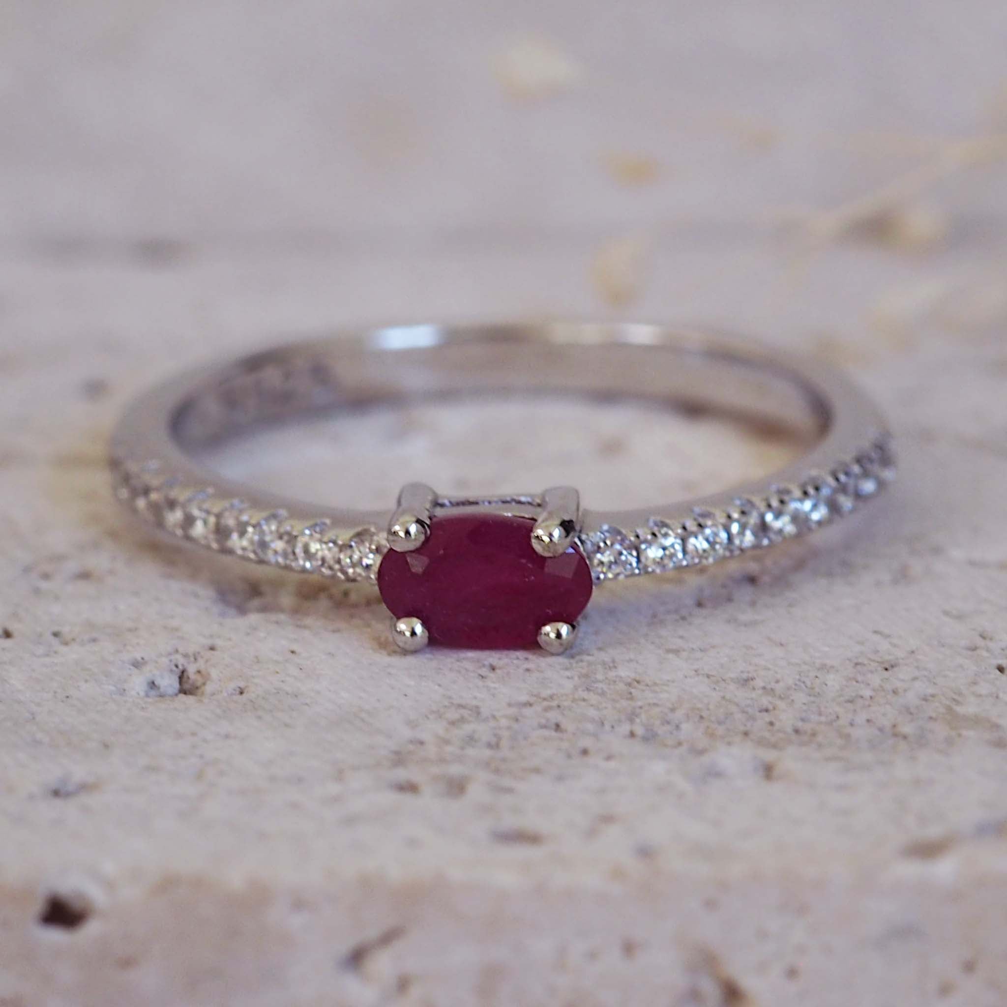 Silver ring with a red gemstone and diamond accents on a textured surface