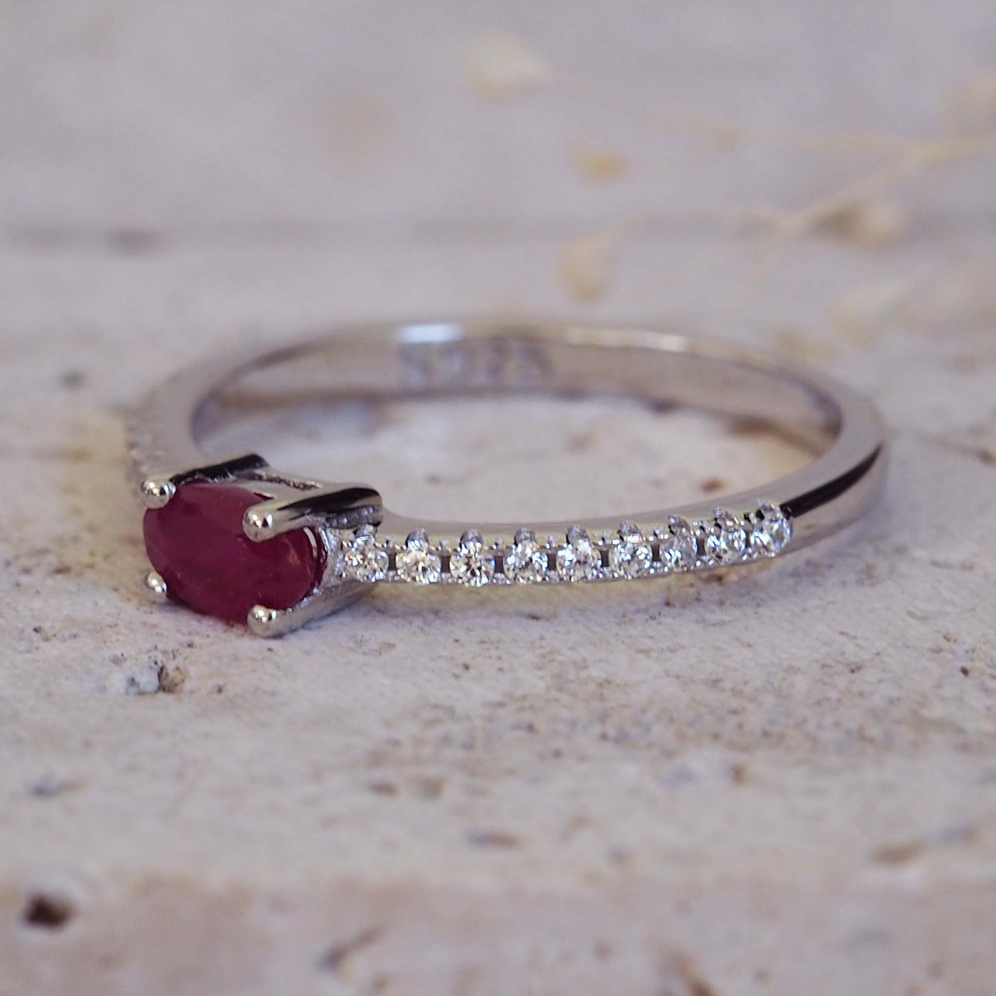 Silver ring with a red gemstone and small diamonds on a textured beige background