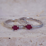 Two silver rings with red gemstones on a textured beige surface