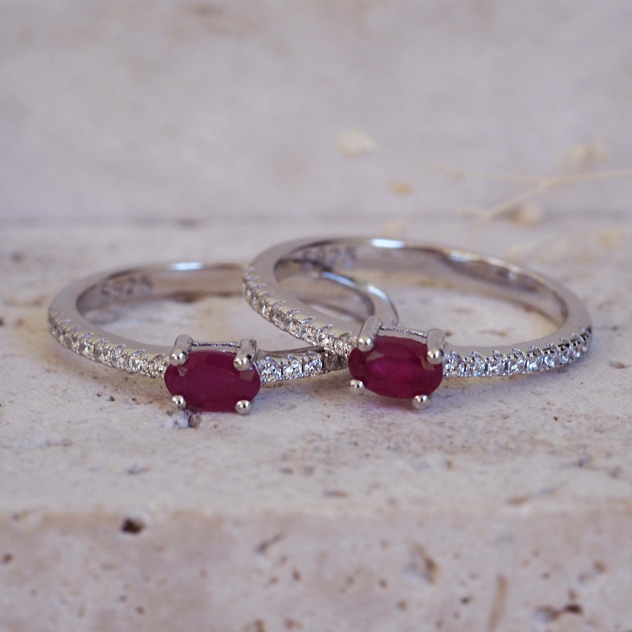 Two silver rings with red gemstones on a textured beige surface