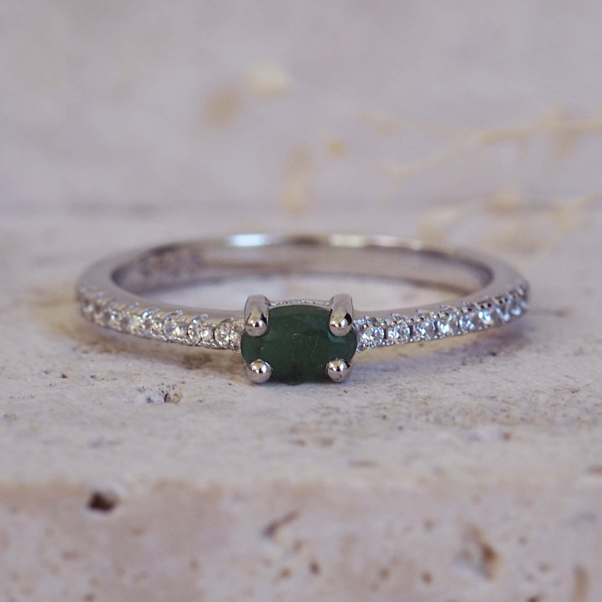 Silver ring with a green gemstone on a textured beige surface