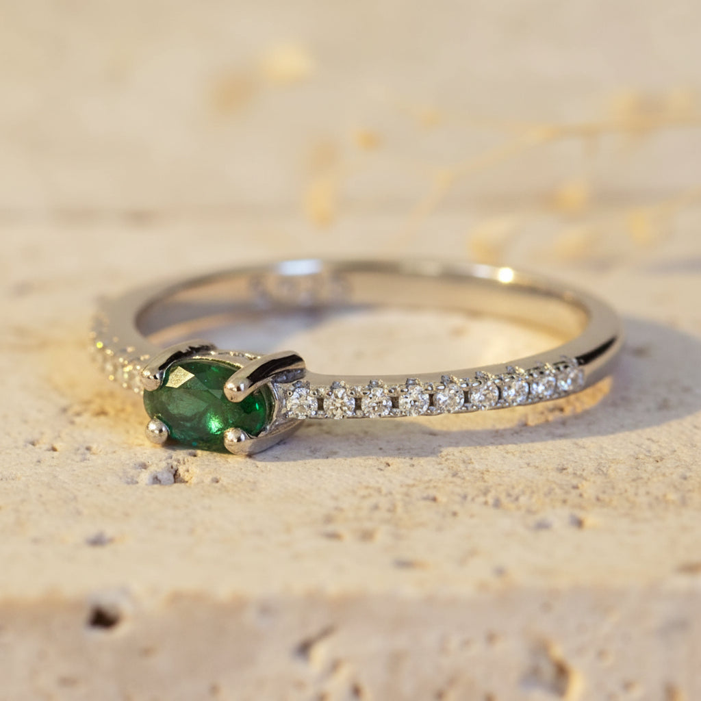 Silver ring with a green gemstone and small diamonds on a textured beige background