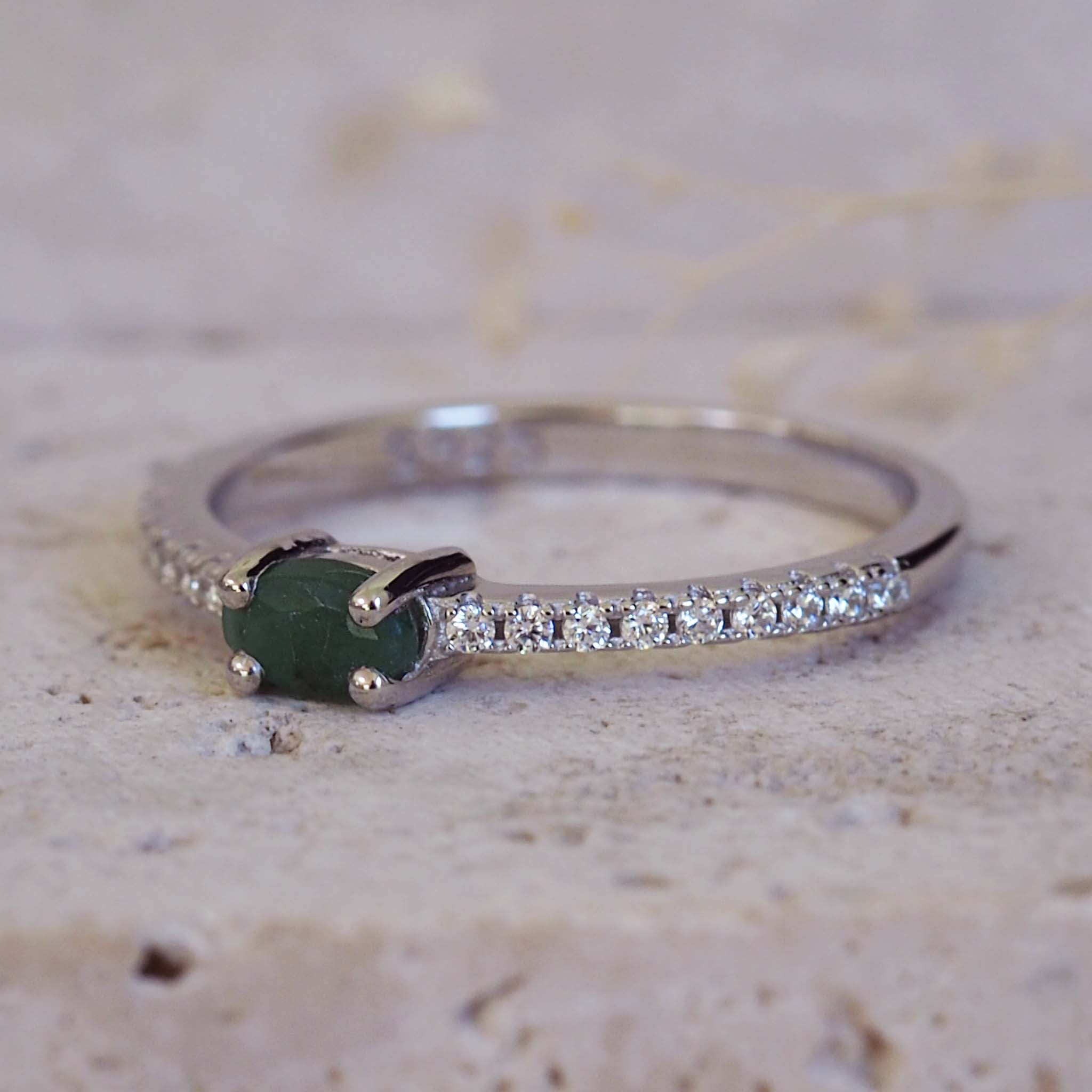 Silver ring with a green gemstone and small diamonds on a textured beige background