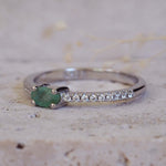 Silver ring with a green gemstone and small diamonds on a textured surface