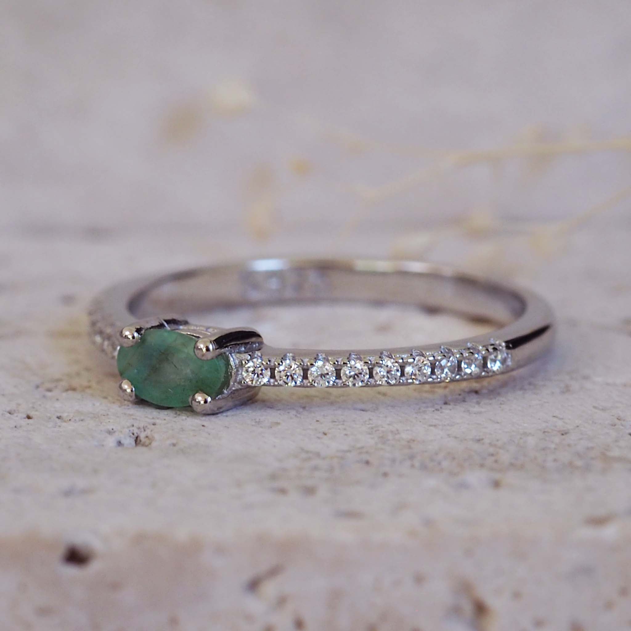 Silver ring with a green gemstone and small diamonds on a textured surface