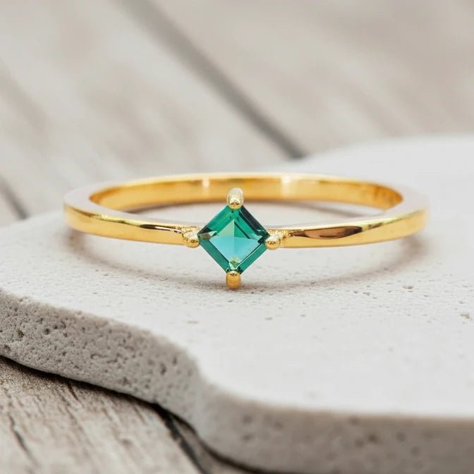 Gold ring with a green gemstone on a stone surface with blurred natural background