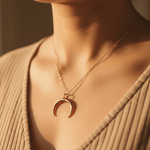 gold crescent moon necklace on a person wearing a beige top.