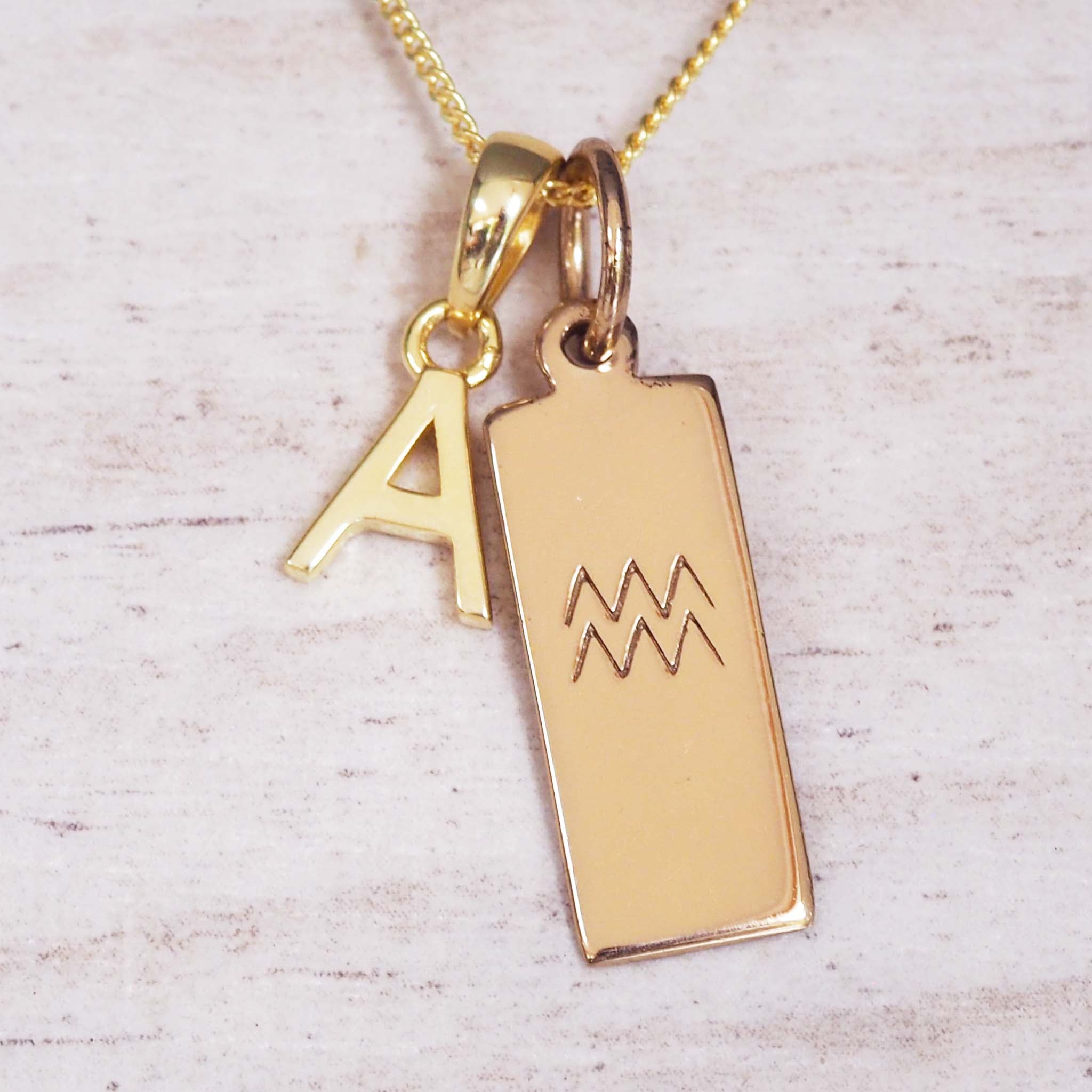 Gold necklace with 'A' pendant and Aquarius symbol on a light wooden background