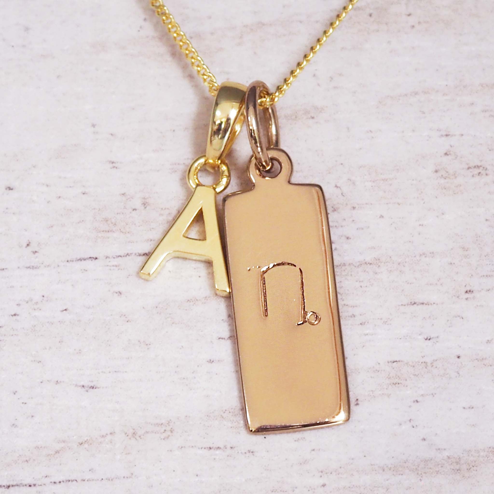 Gold necklace with a pendant featuring the letter 'A' and a symbol on a light wooden background