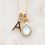 Gold necklace with 'A' initial pendant and a march birthstone natural aquamarine gemstone pendant on a beige background