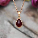 Gold necklace with a red teardrop pendant on a blurred background