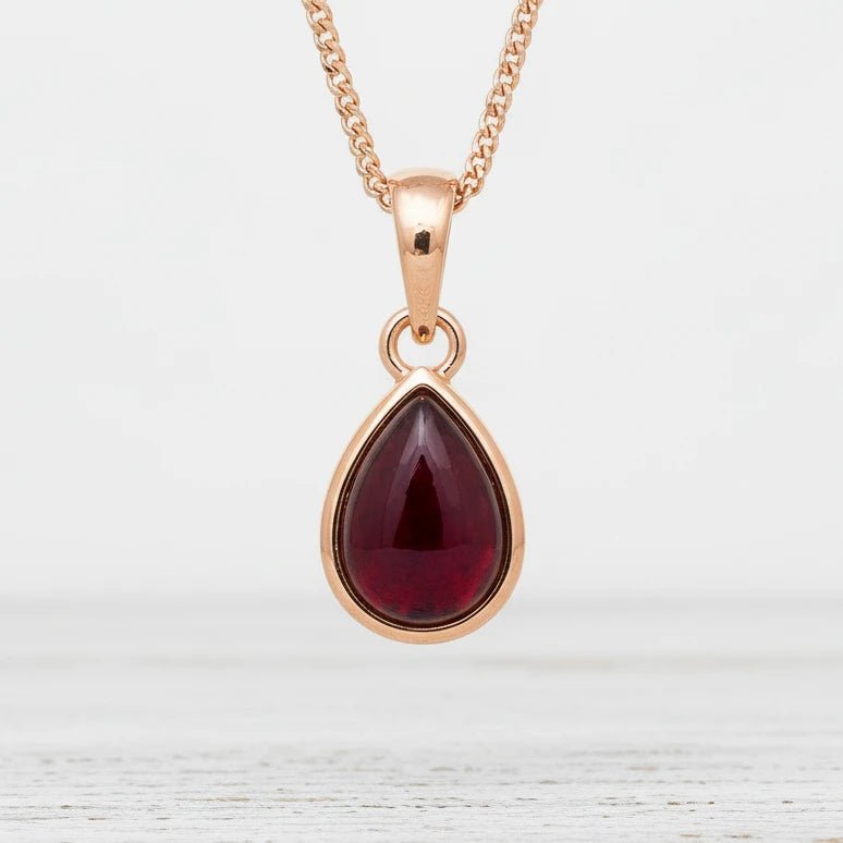 Gold necklace with a red teardrop pendant on a blurred background