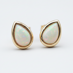 Teardrop-shaped opal earrings with gold setting on a light gray background
