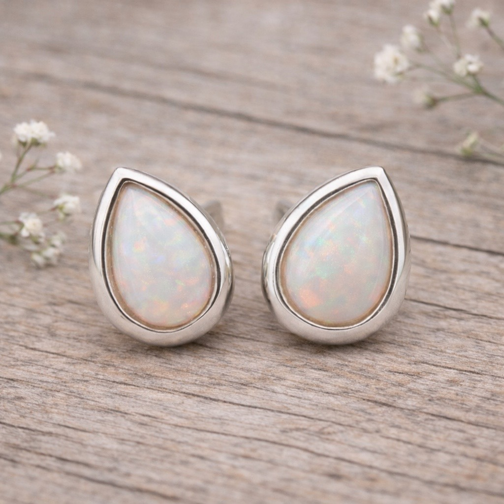 Teardrop-shaped opal earrings with silver setting on a light gray background