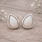 Teardrop-shaped opal earrings with silver setting on a light gray background