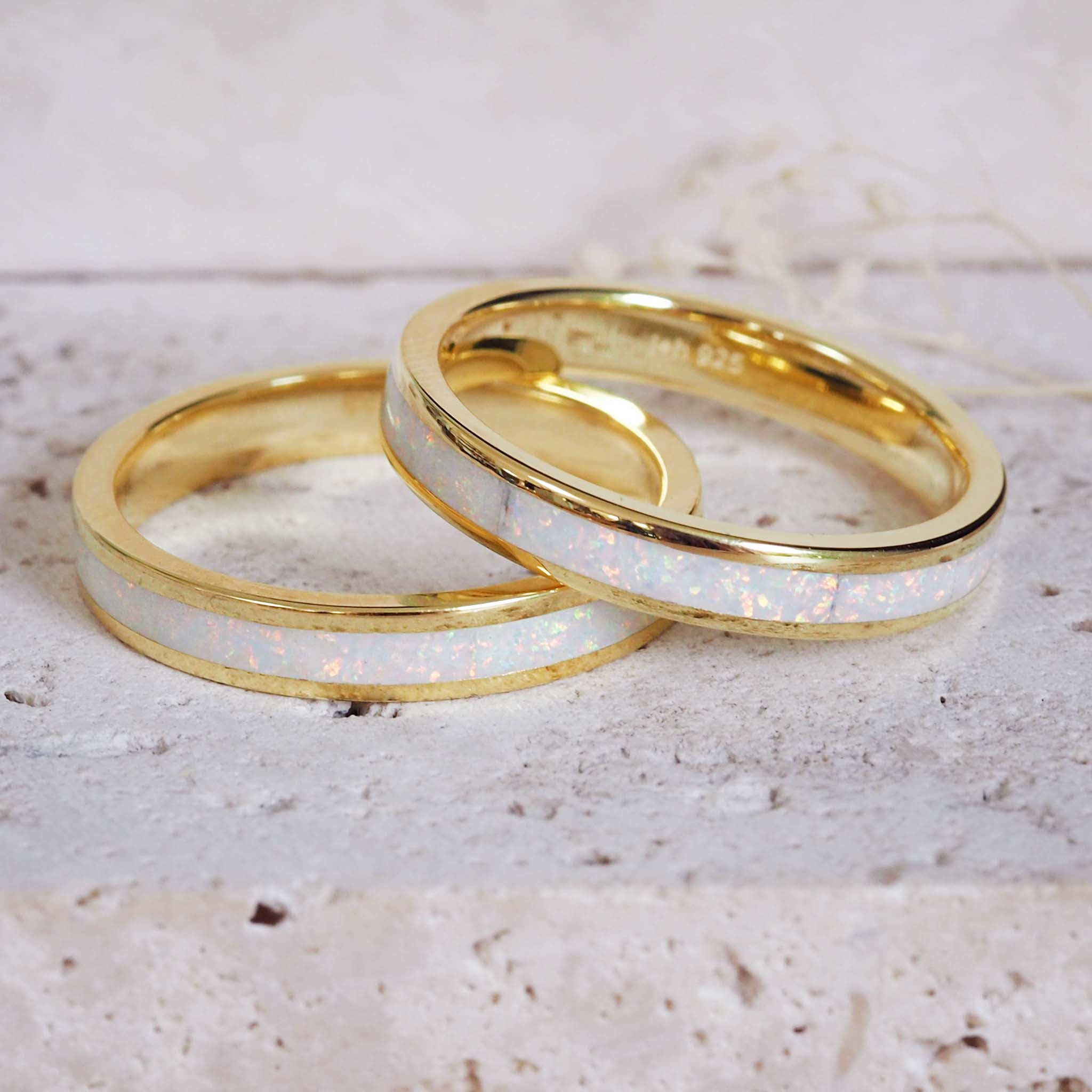 Two gold rings with white inlay on a light surface