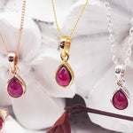 Three necklaces with teardrop-shaped ruby pendants on a marble surface.
