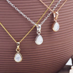 Three necklaces with teardrop pendants on a brown textured surface