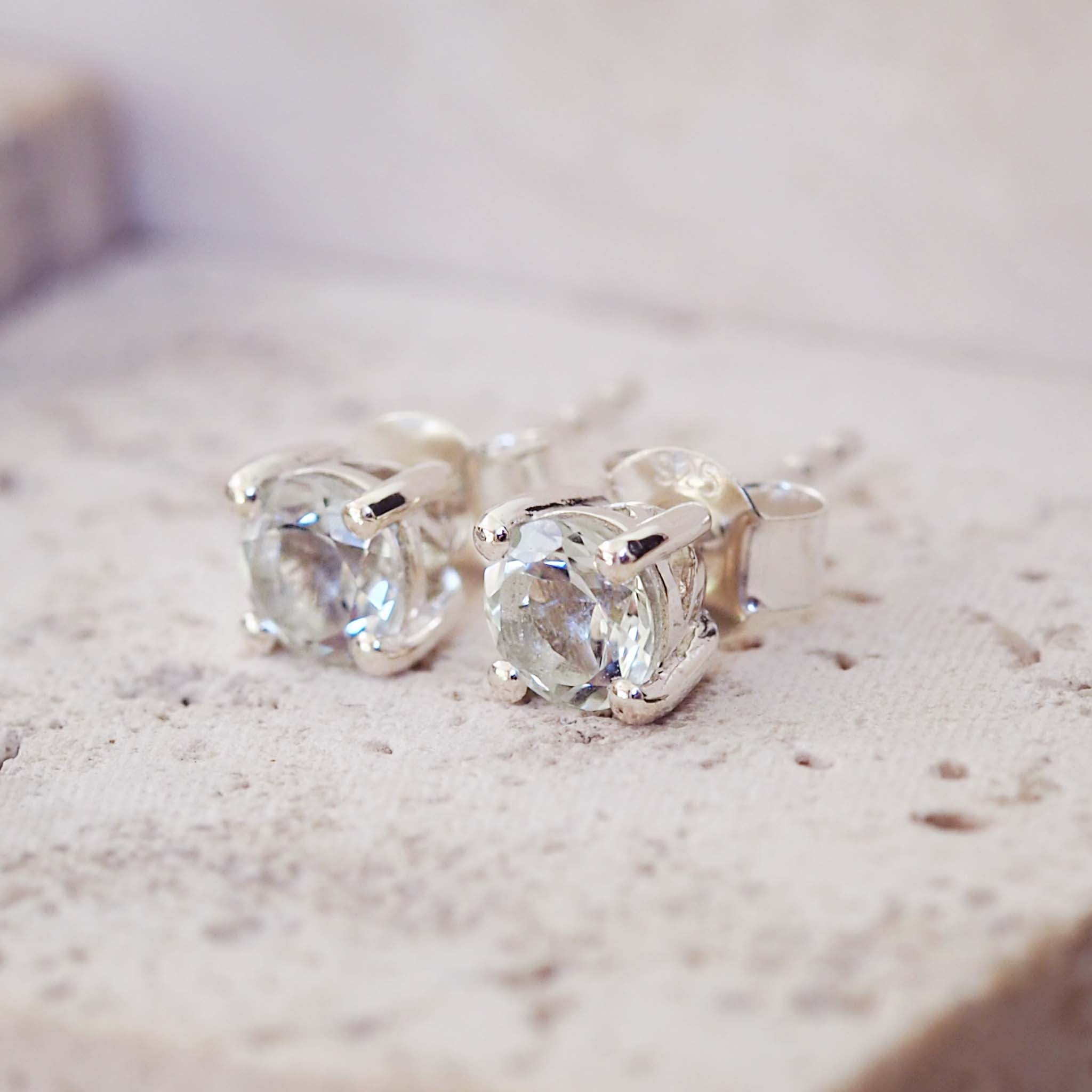 Silver earrings with clear gemstones on a textured surface