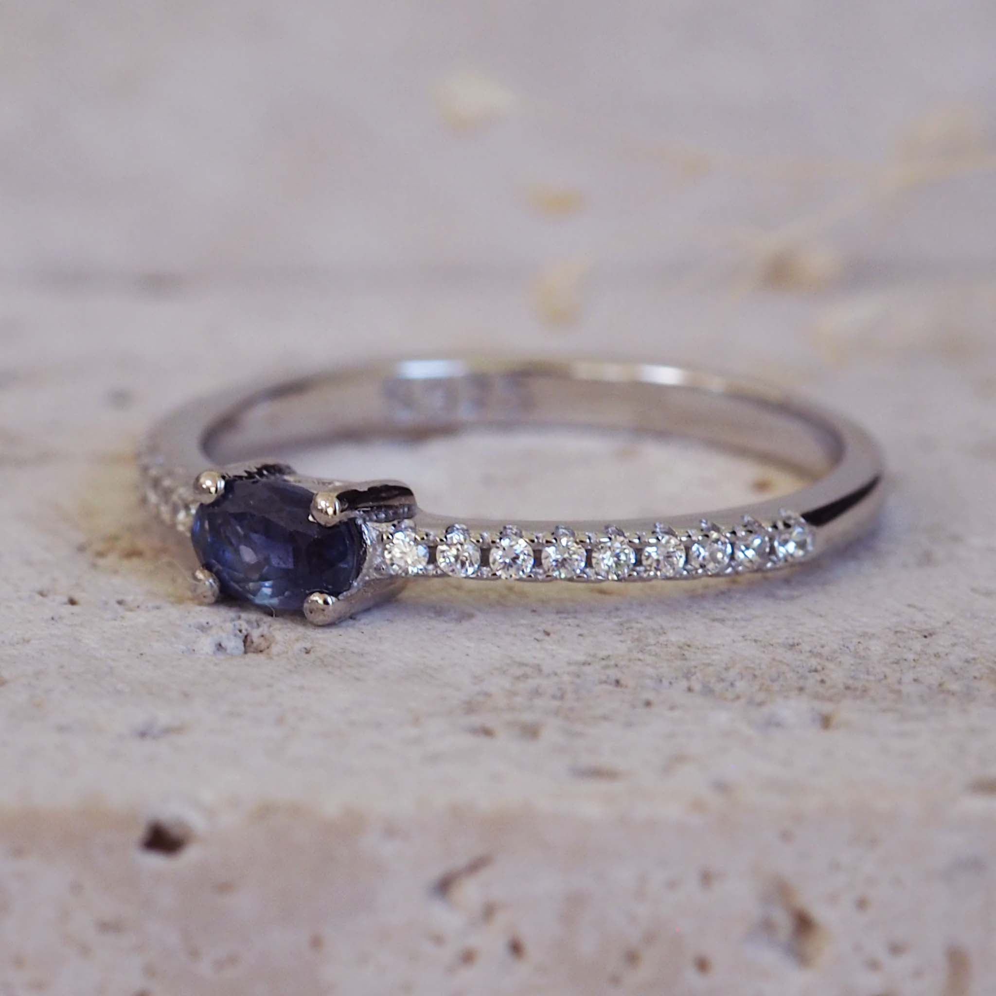 Silver ring with a blue gemstone and small diamonds on a beige surface