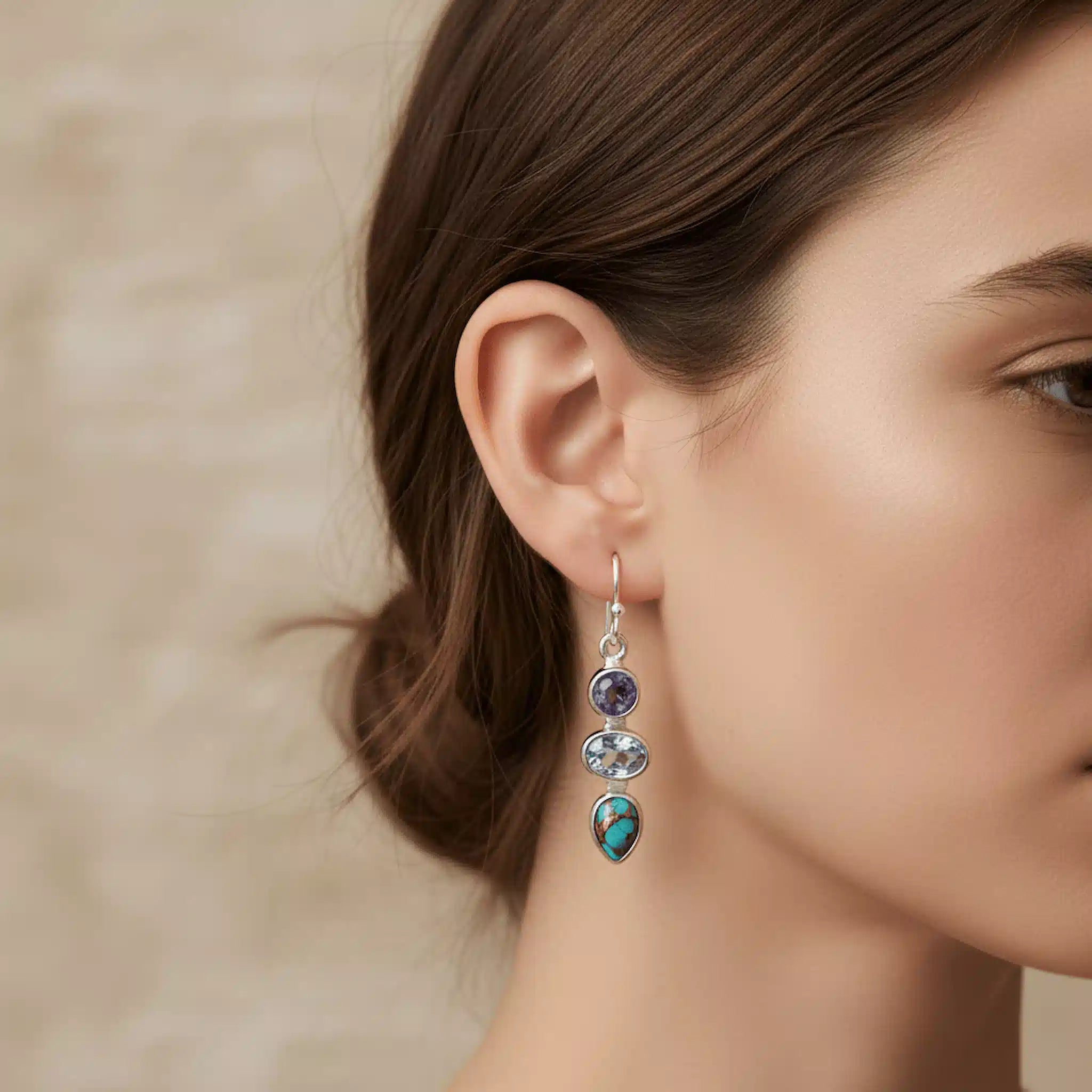 Close-up of a woman wearing a silver earring with colored stones against a neutral background