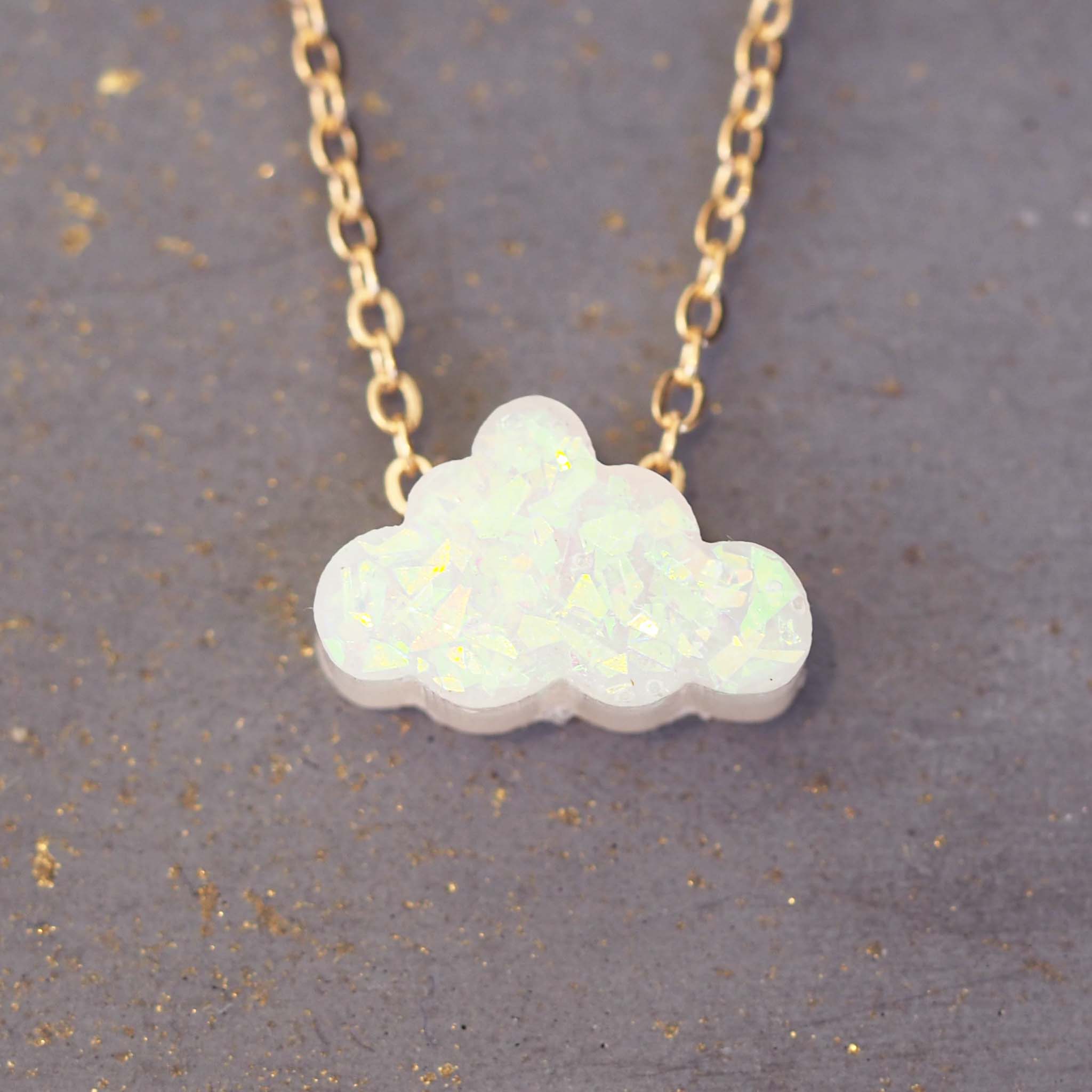 Opal cloud-shaped pendant on a gold chain against a gray background