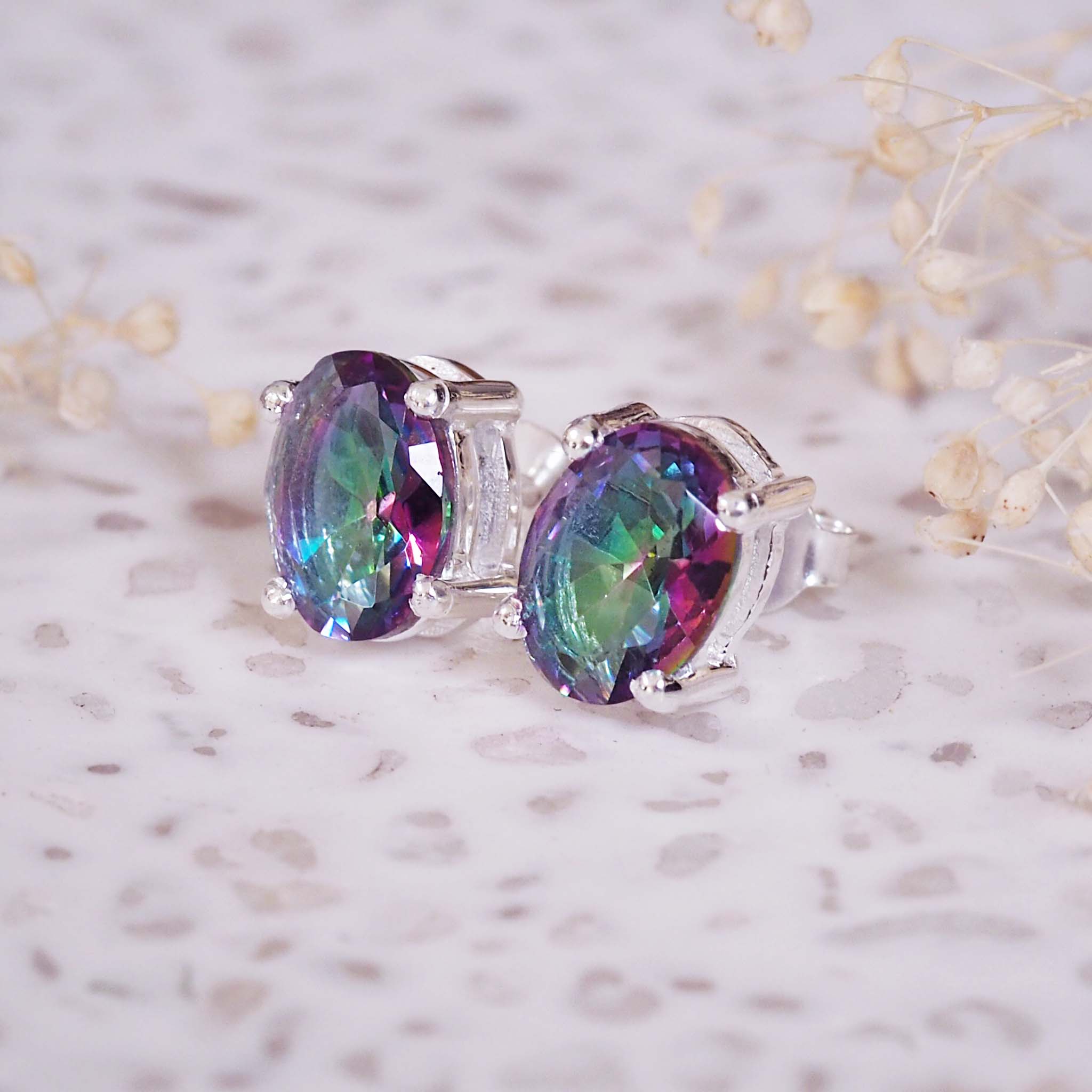 Multicolored gemstone earrings on a light background with dried flowers.