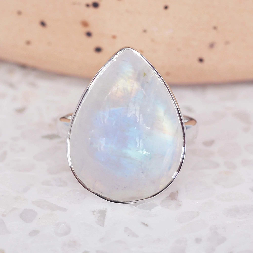 Teardrop-shaped rainbow moonstone ring on a marble surface