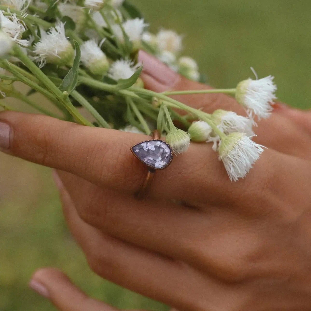 Hand holding a bouquet of white flowers with a ring featuring a purple gemstone.
