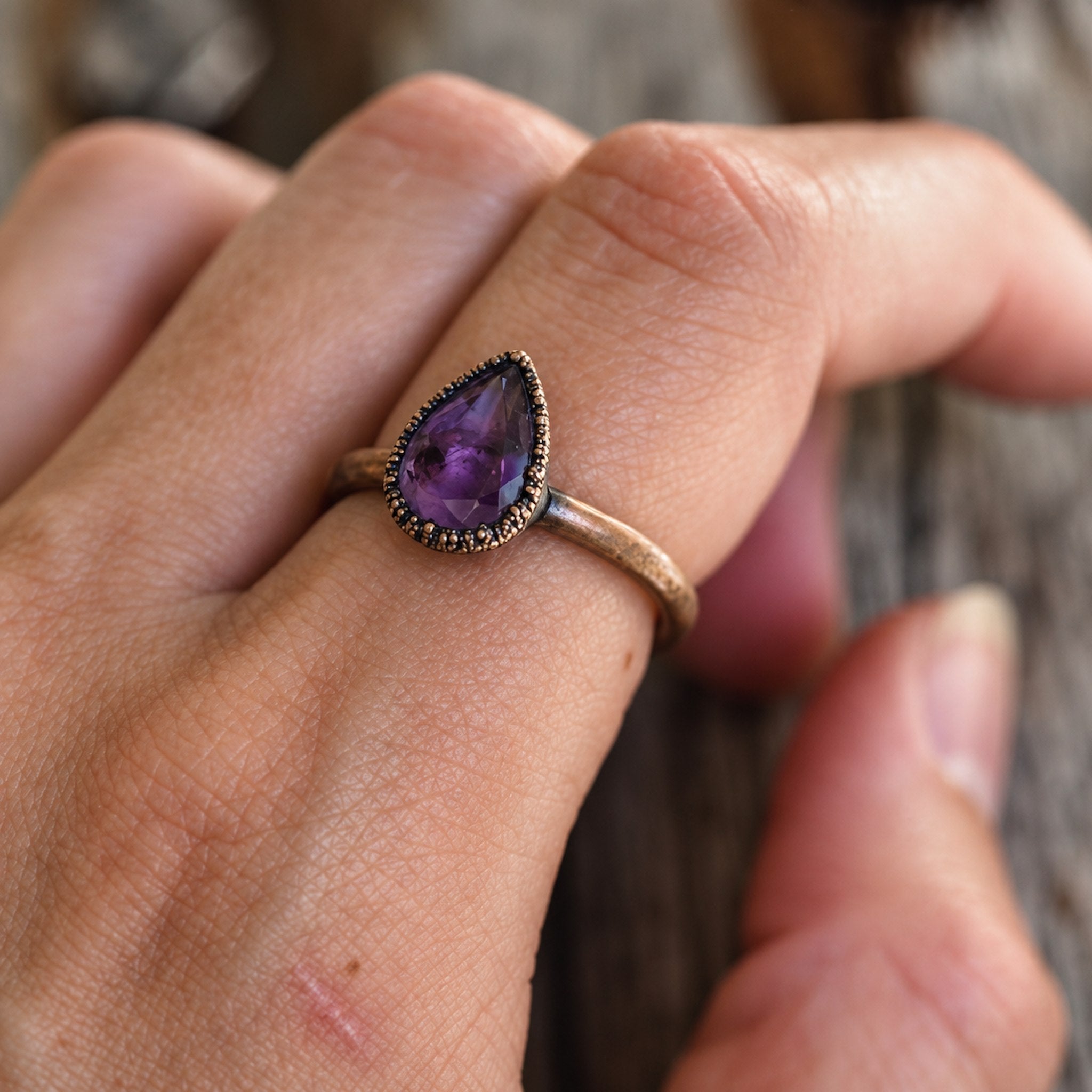 Hand wearing a ring with a purple gemstone on a blurred background