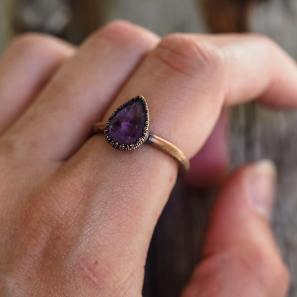 Hand wearing a ring with a purple gemstone on a blurred background