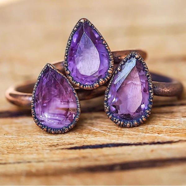 Ring with teardrop-shaped purple gemstones on a wooden surface