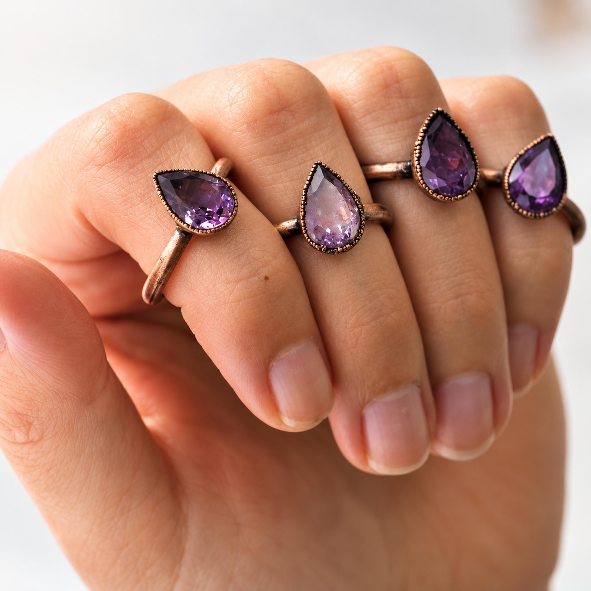 Hand wearing multiple rose gold rings with purple gemstones on a white background