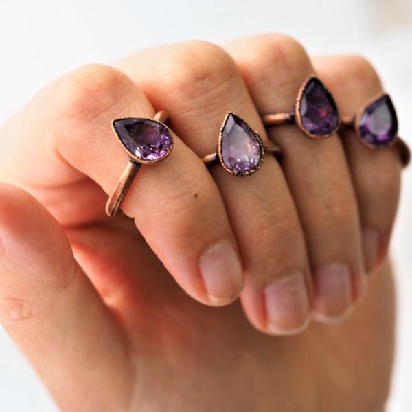 Hand wearing multiple rose gold rings with purple gemstones on a white background