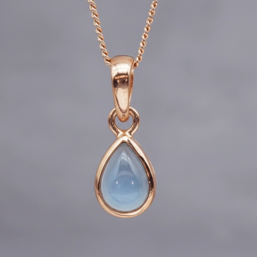 Rose Gold pendant with a blue teardrop-shaped topaz gemstone on a gray background