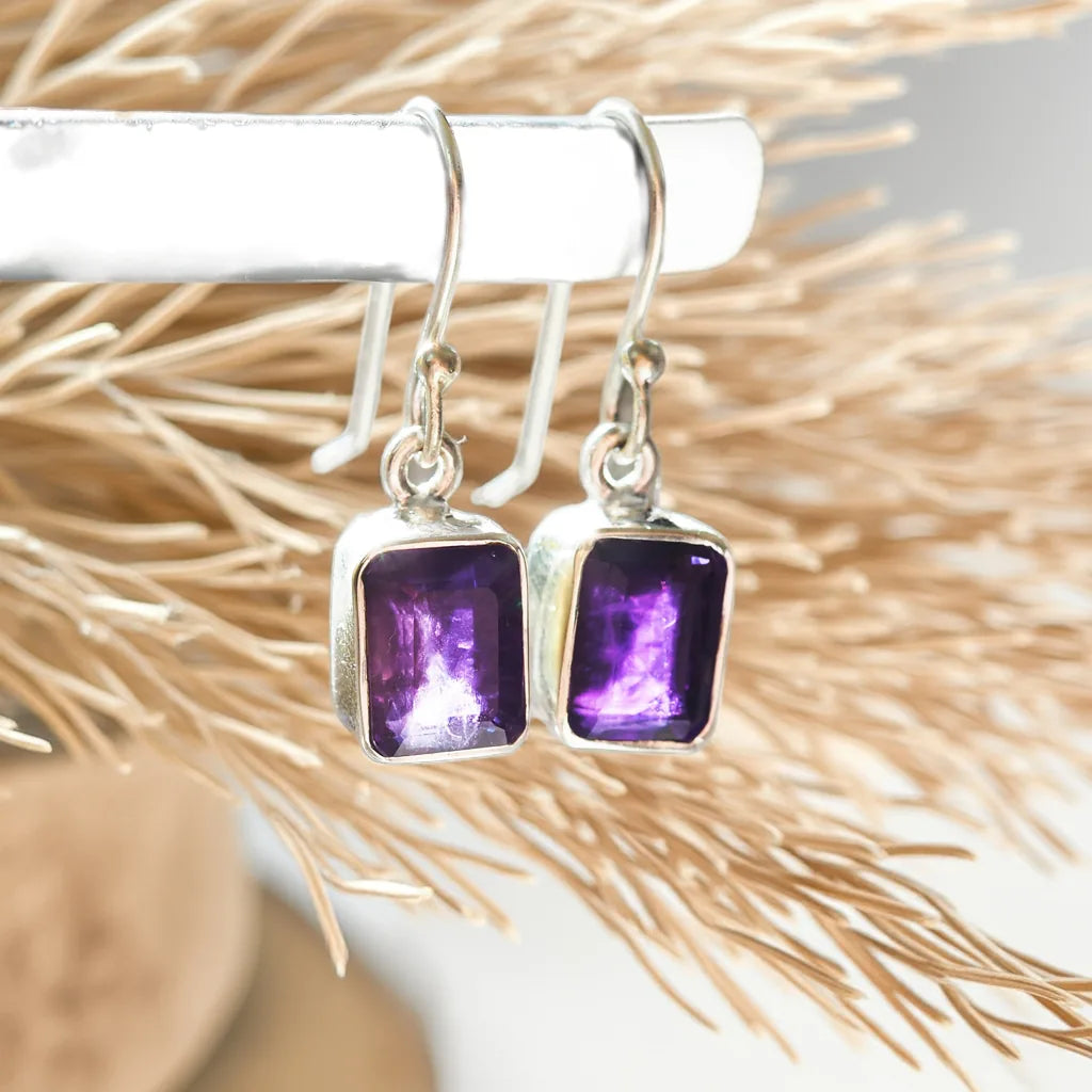 Silver earrings with purple gemstones on a decorative background